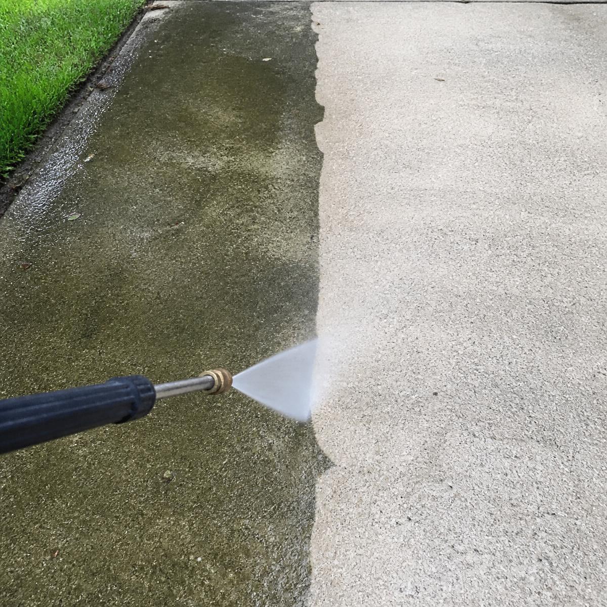 Pressure washer cleaning a grimy concrete driveway back to bright concrete